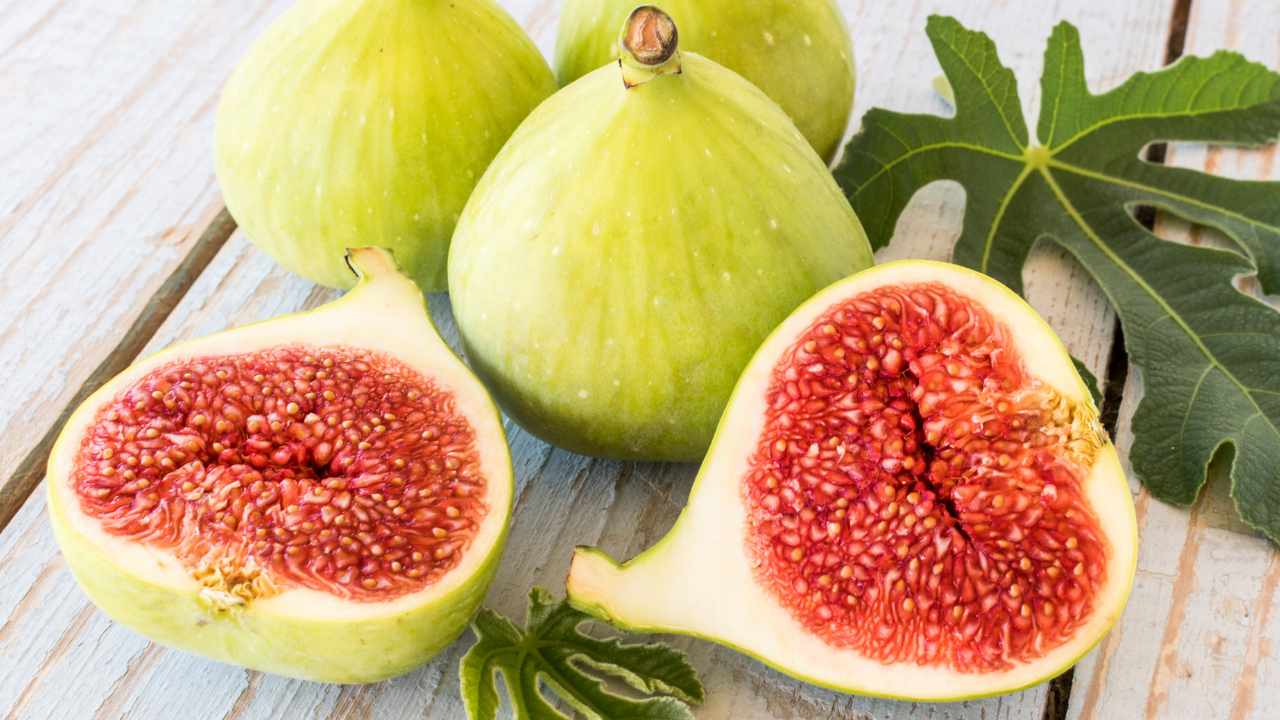 green figs, sliced figs and leaves on a table