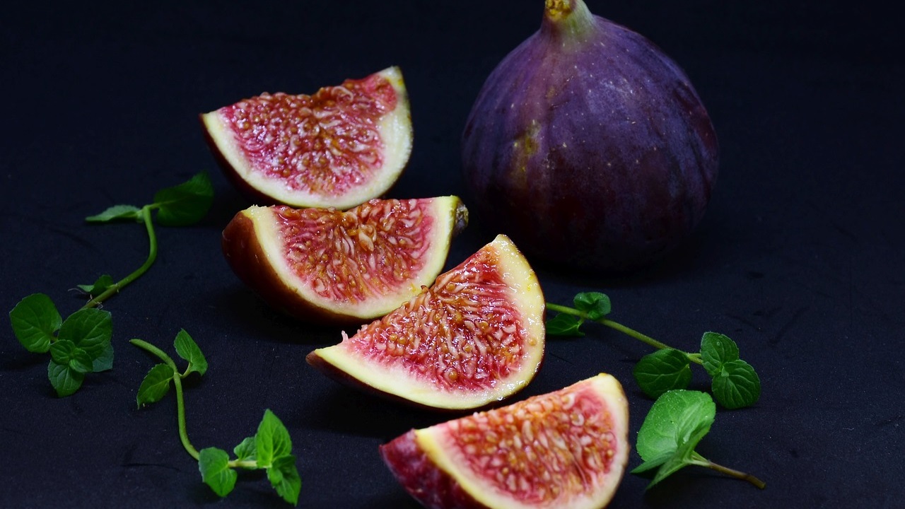 a purple fig, sliced fig and some leaves on a table