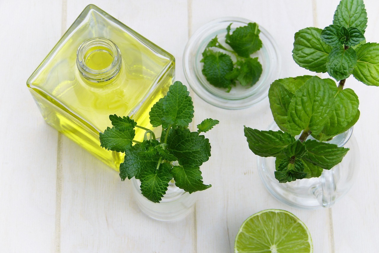 essential oil in a jar, some mint leaves and a lemon on a table