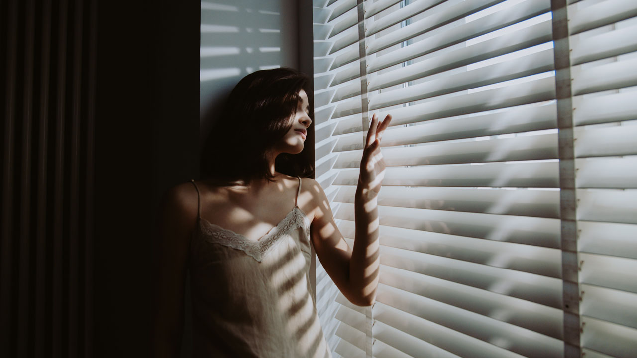 woman looks out shutters