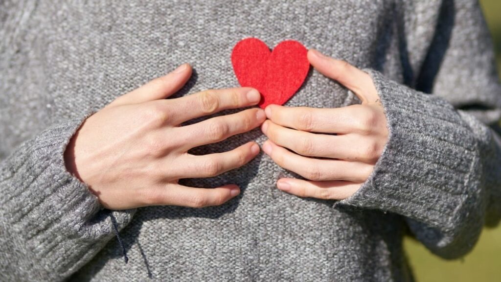 a girl is placing heart symbol at her chest urging us to take care of our heart