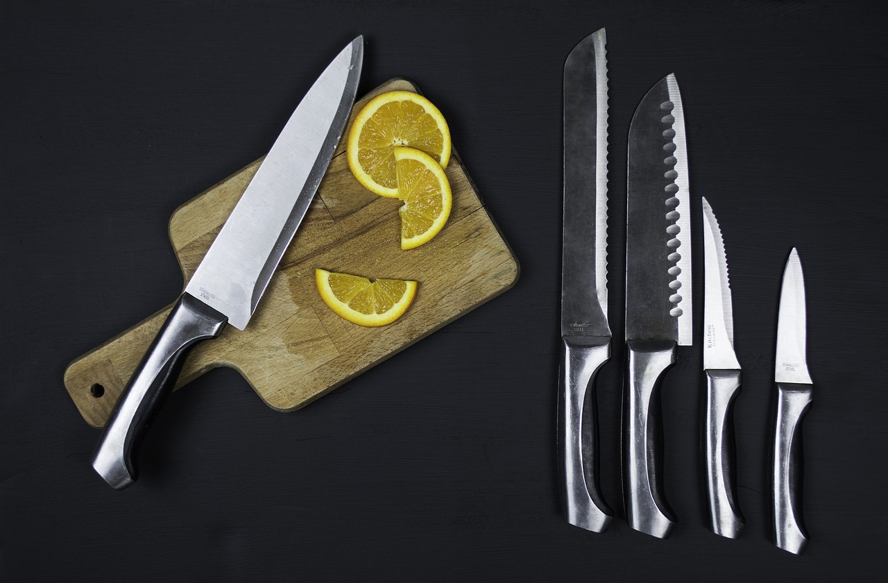 sliced lemon and knife is placed on a vegetable cutting table and a pair of knives are placed beside them on the table