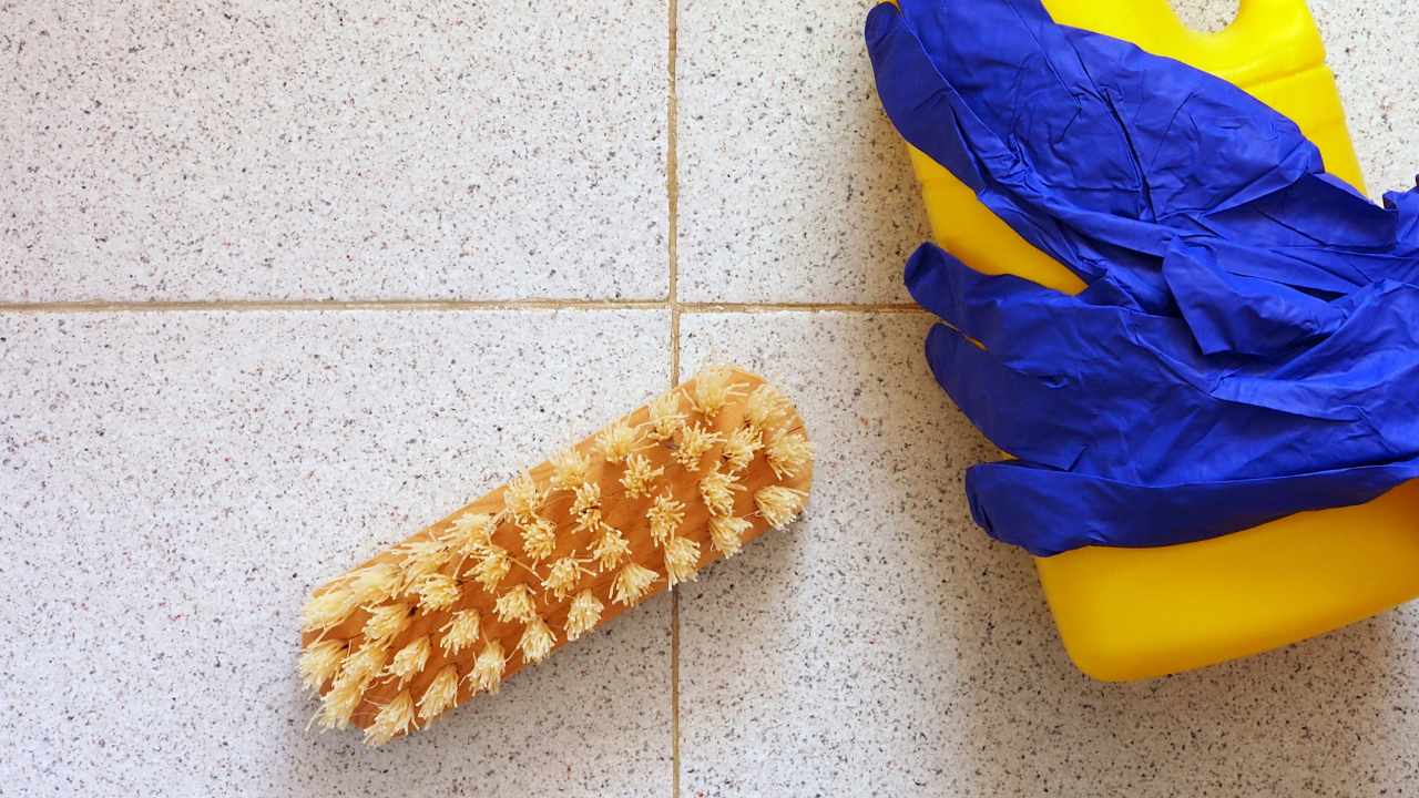 solution in a bottle, brush and pair of gloves are placed on the floor