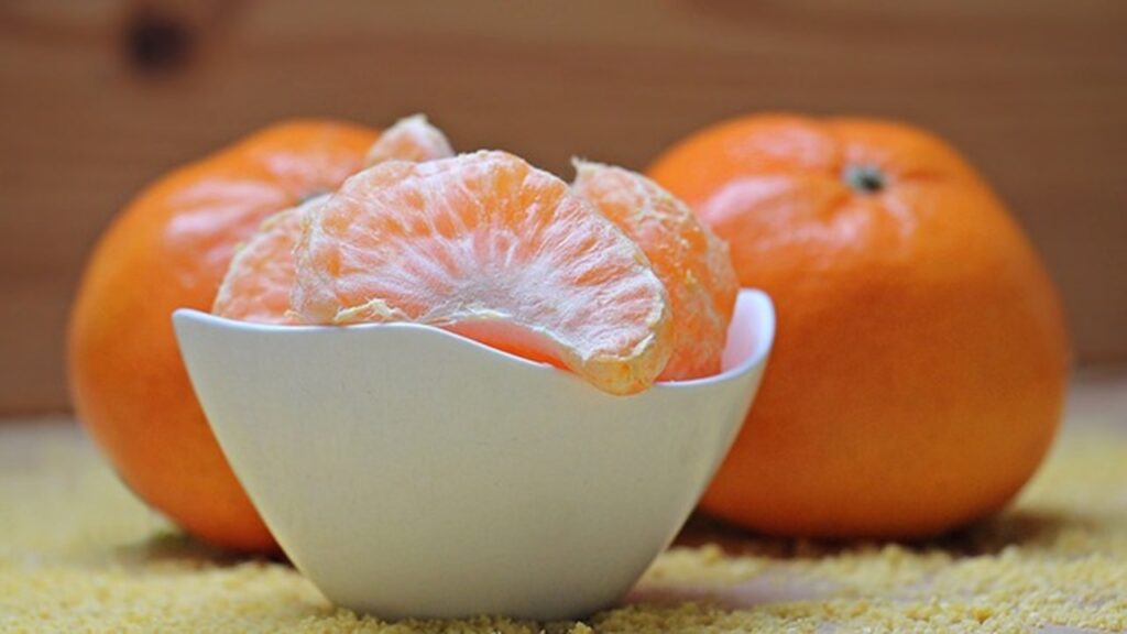a clementine is in a bowl peeled off with other 2 placed beside it on the table