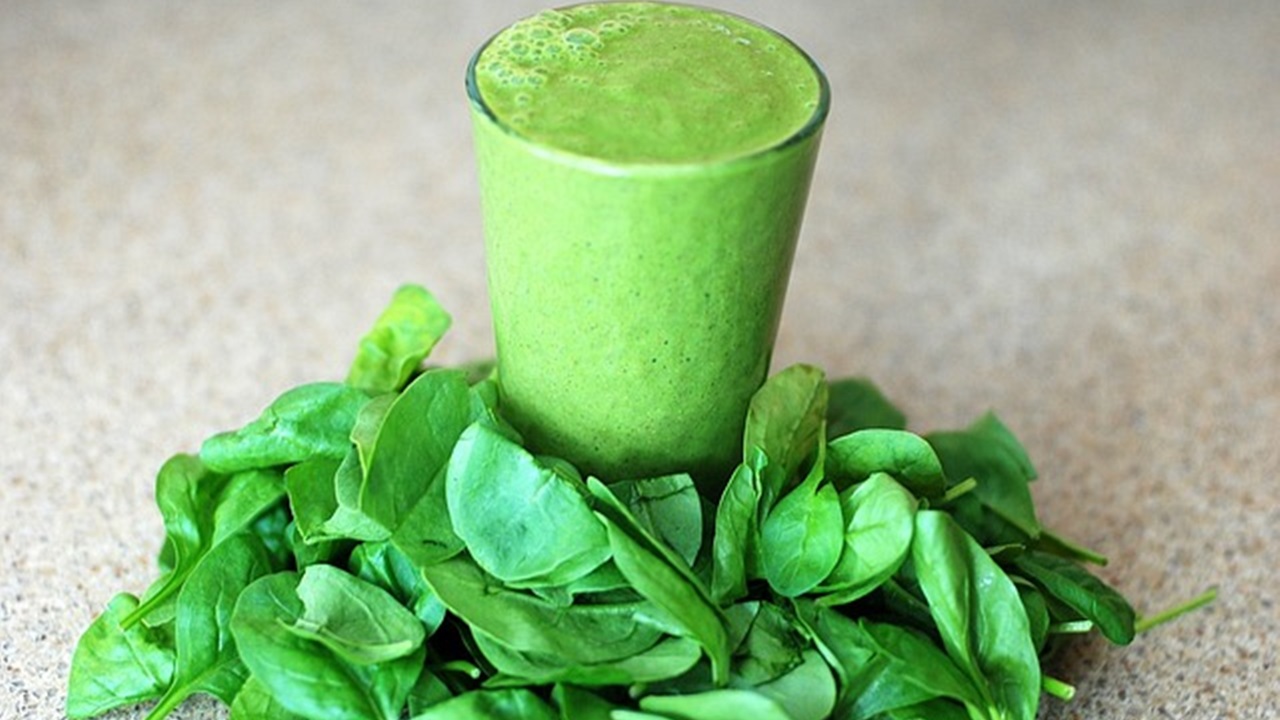 spinach juice in a glass and some spinach leaf placed on a table