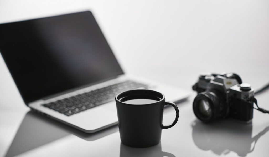 laptop, camera and a healthy apple rosemary drink in a cup are placed on the table