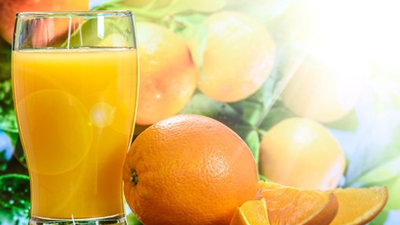 a glass of orange juice and sliced oranges are placed on a table