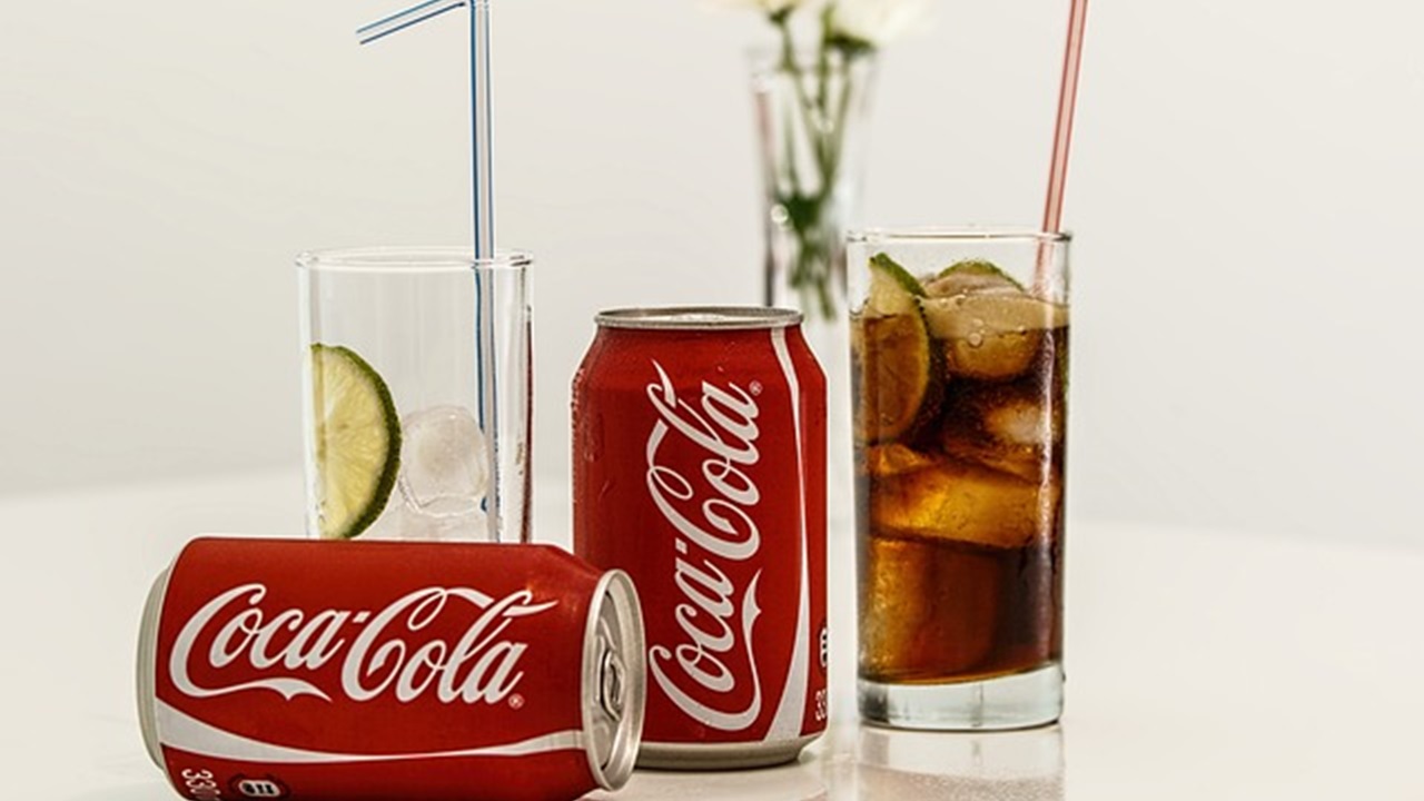 2 coca cola cans and a glass filled with coca cola
