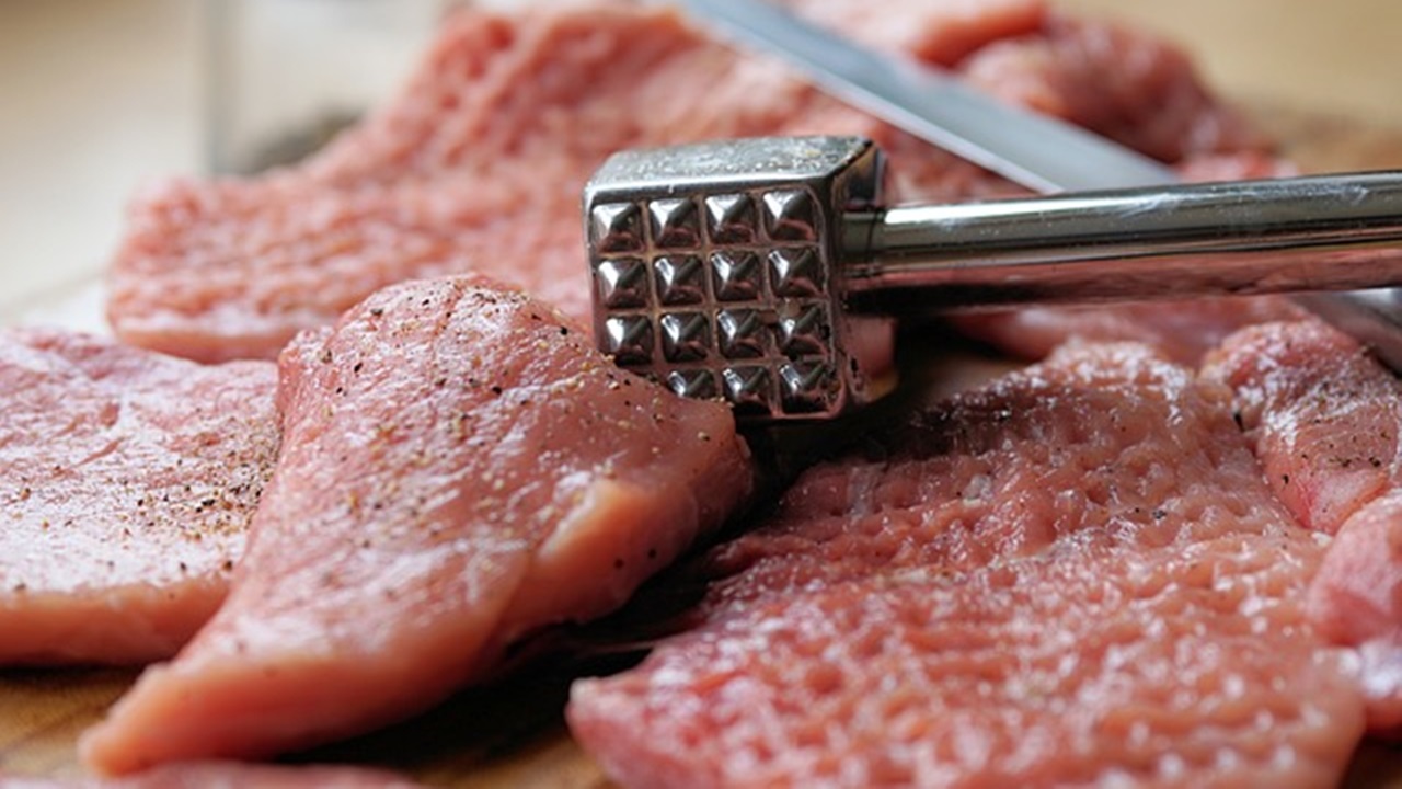 a person is beating the veal slices to tenderize them