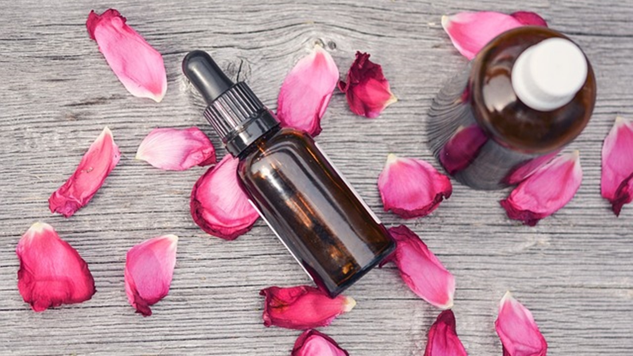 bottle of perfume and some petals of rose are placed on the table