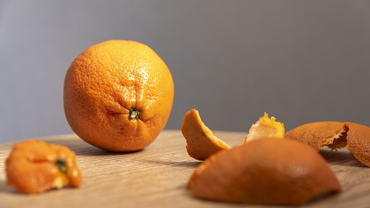 an orange and some peels of it are placed on the wooden table