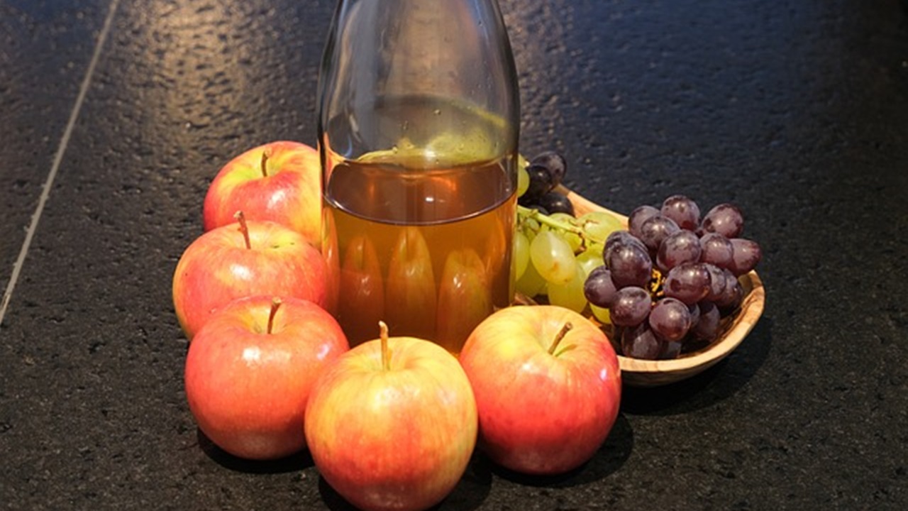 some apples, grapes and a bottle of apple cider vinegar are placed on the table