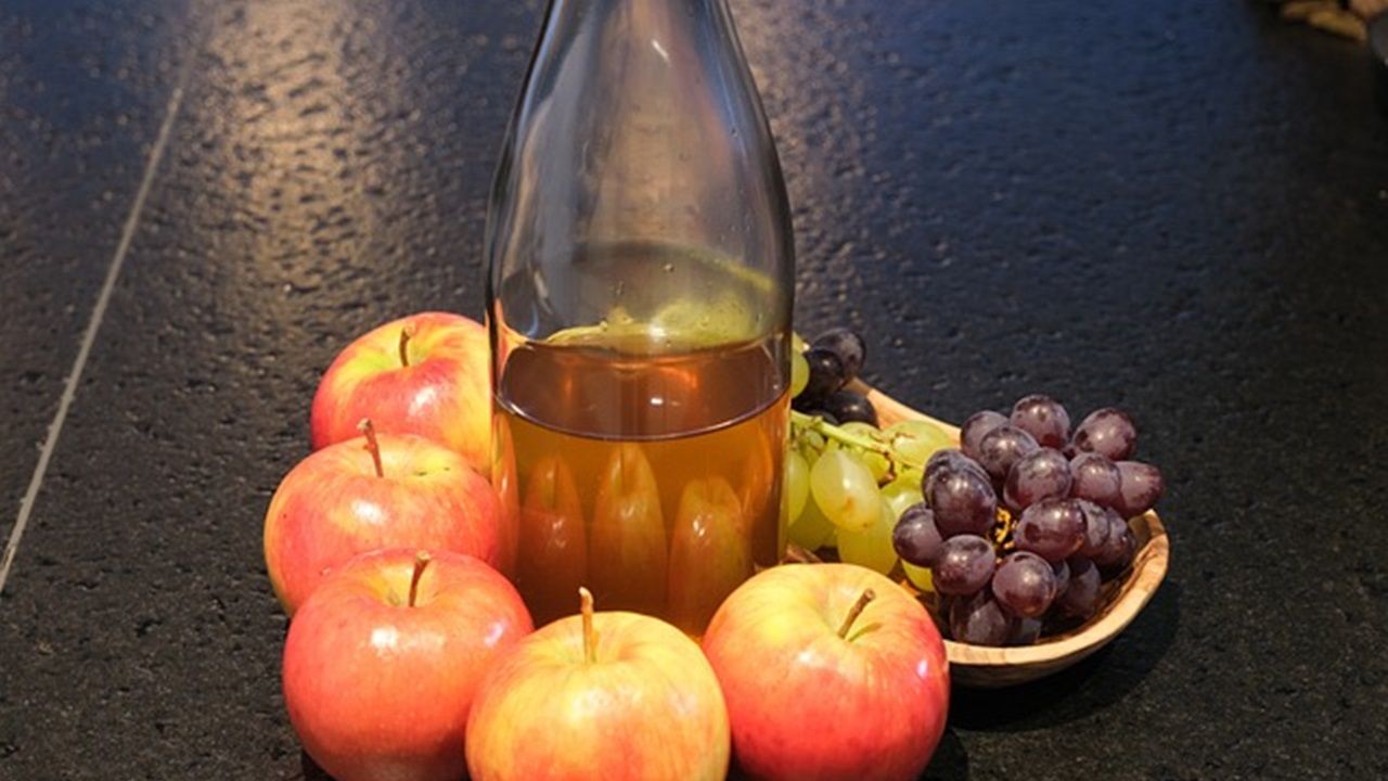 some apples, grapes and a bottle of apple cider vinegar are placed on the table